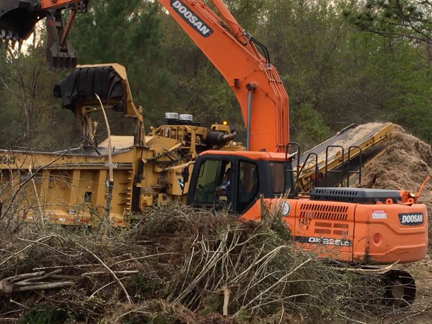 One of GEC's excavators dropping tree limbs into a stump grinder